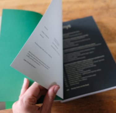 The photo shows the pages of a book being turned. The three main colours used in the book are asphalt grey, creamy white and 