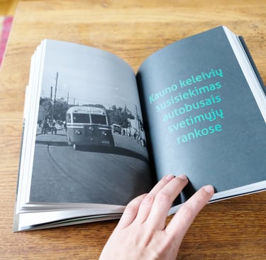 The photo shows the pages of a book being turned. A photograph of a vintage bus and the title of the column "Kaunas passenger