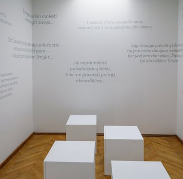 Nieko neveikimo akademijos erdvė. Sienos baltos, išklijuotos pilkos spalvos lipdukais su Mikučio mintimis. Ant grindų išdėlio