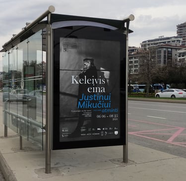 Plakatas mieste, autobusų stotelėje. Plakato dizianas išlaikytas toks pats kaip pagrindinio plakato.