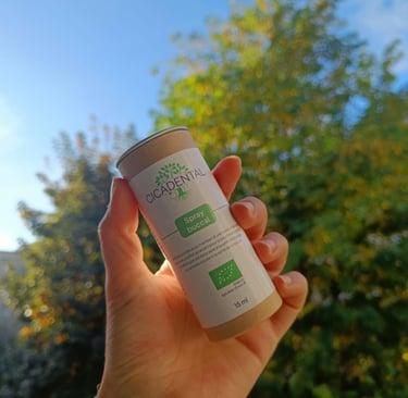 Hand holding a bottle of Cicadental organic buccal spray against a natural green tree background.