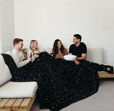a group of 4 friends enjoying a drink together under one big extra large blanket