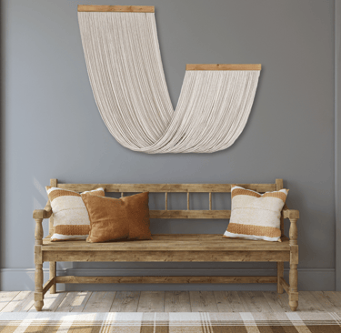 A Wall Hanging Made with Cotton Rope Suspended from Wooden Board that is Hung Above a Wooden Bench