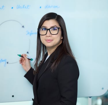 Ka Ming Zwingenberger in a suit and glasses standing in front of a white board with a marker..
