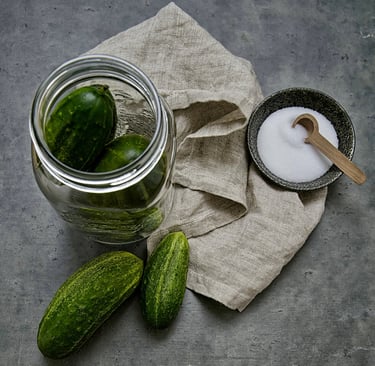 a jar of small cucumbers with a bowl of salt and a linen cloth