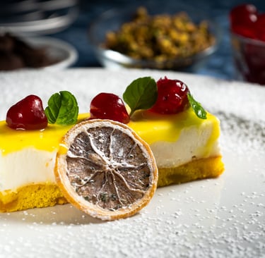 Due fette di torta gialla con crema bianca, glassa gialla, ciliegie rosse, menta e arancia essiccata