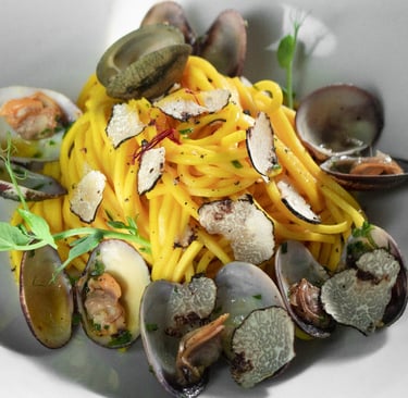 Spaghetti con vongole e tartufo in piatto bianco, con conchiglie aperte e germogli verdi
