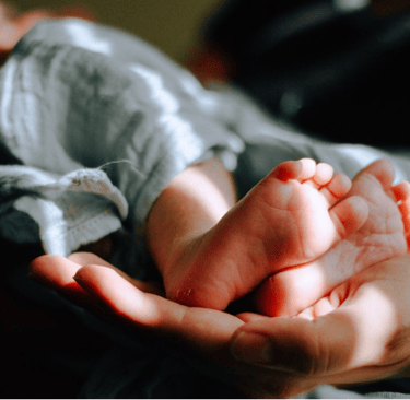 Eine Person hält Baby_Füße in der Hand