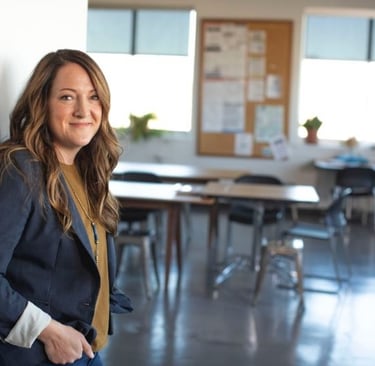 a female teacher standing in a room with a desk and chairs