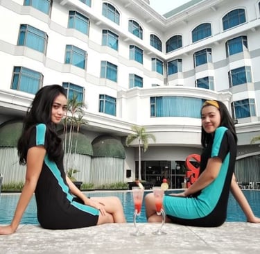 two hospitality workers in blue dresses sitting by a hotel swimming pool 