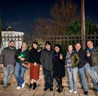Group of eight tourists posing with peace signs and green flashlights in front of ornate iron fence during Athens Ghost Tour