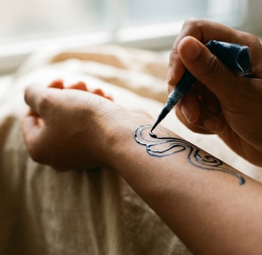Close-up of a person applying a black henna ink temporary tattoo design to their forearm with an applicator.
