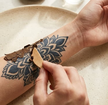 Applying a natural herbal paste over a mandala tattoo with a wooden spatula for skin care.