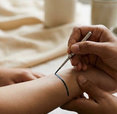 A person applying a blue temporary tattoo or body art ink to a wrist using a fine-tipped metal tool.