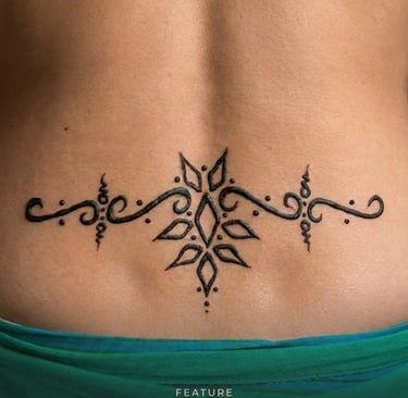 Elegant black ink ornamental tattoo design on a person's lower back featuring symmetrical floral patterns.