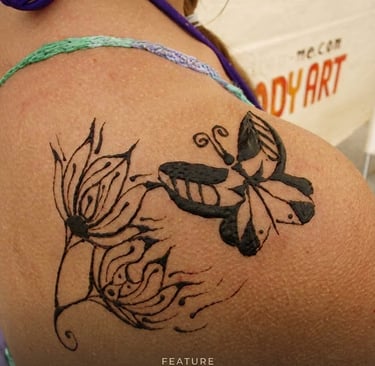 A delicate black butterfly and floral henna tattoo design applied to a woman's shoulder.