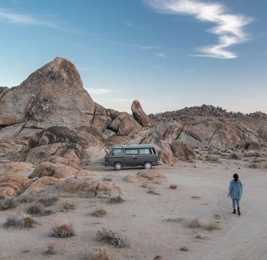 A van parked in near a small mountain and a person walking towards it.