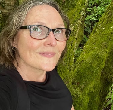 a woman in glasses and a black shirt is taking a selfie in nature