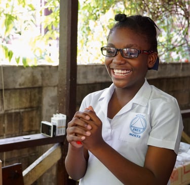 A smiling young female student wearing glasses and a white school uniform with a logo.