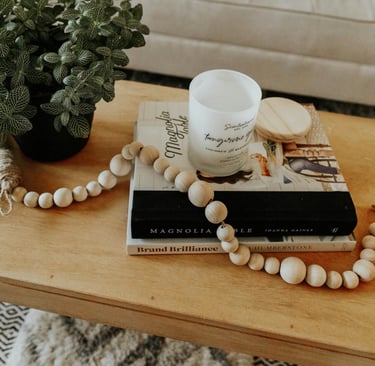 wooden table with a potted plant, a pile of books, a candle and a wooden bead garland
