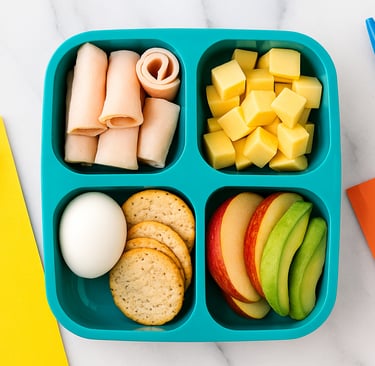 Overhead flat lay of divided lunchbox with turkey roll-ups, cheese cubes, egg, crackers, apple slice