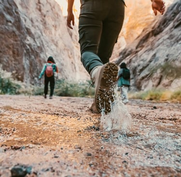 3 people walking through a canyon, boots stomping in the mud