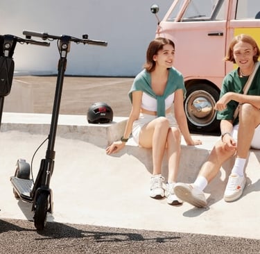 two women sitting on a skateboard in front of a van