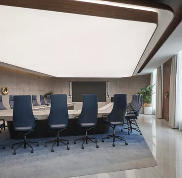 Modern corporate boardroom with a large conference table, blue ergonomic chairs, and professional office lighting.