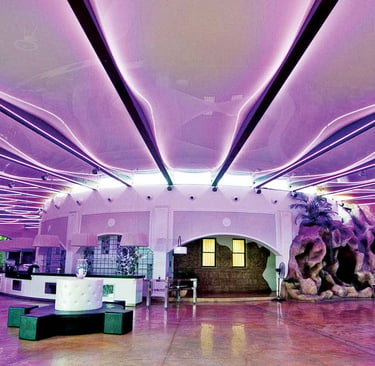 Modern lounge interior featuring wavy purple LED ceiling lighting and artificial rock formations.