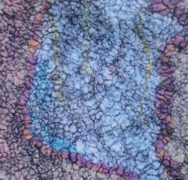 A textured piece of handmade felt art featuring blue, purple, and gray wool fibers in a bubbly pattern.
