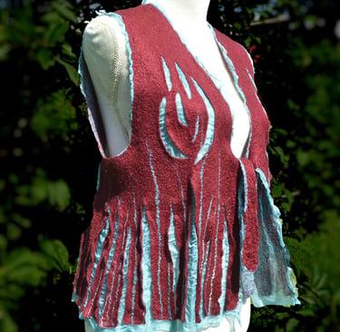 Handmade burgundy and turquoise nuno felted wool vest with fringe details on a mannequin outdoors.