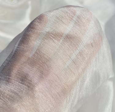 A hand visible through a layer of sheer, white shimmering silk fabric texture.