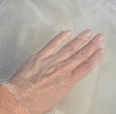 A person's hand touching fine white sheer organza fabric, showcasing its delicate mesh texture.