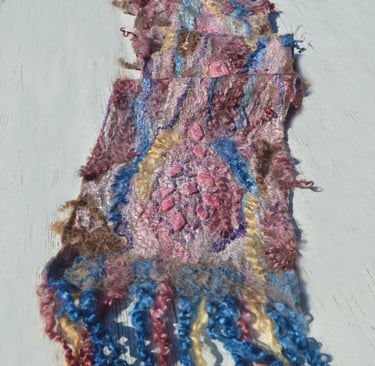 Handmade nuno felted scarf with colorful wool fibers and silk textures on a white wooden surface.