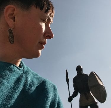 A profile view of a woman in a blue sweater near a historical warrior statue with a shield and spear.