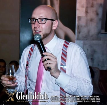 a man in shirt and tie presenting a whisky tasing with a microphone