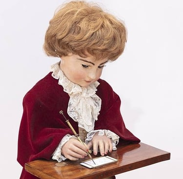 Vintage mechanical writing automaton doll in a red velvet coat sitting at a wooden desk.
