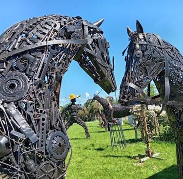 Metal scrap art sculpture of two horse heads made from recycled tools and gears in a park.