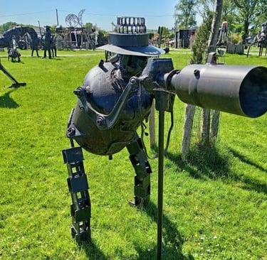 Metal scrap sculpture of a robot photographer with a camera in an outdoor art garden.