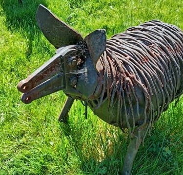 Rustic scrap metal pig sculpture handcrafted from recycled iron parts in a green grassy field.