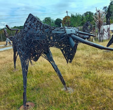 A metal bull sculpture made of recycled scrap metal parts standing in a grassy field.