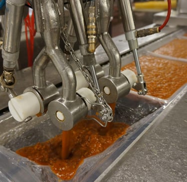Industrial food processing machine filling plastic trays with red pasta sauce on a conveyor belt.