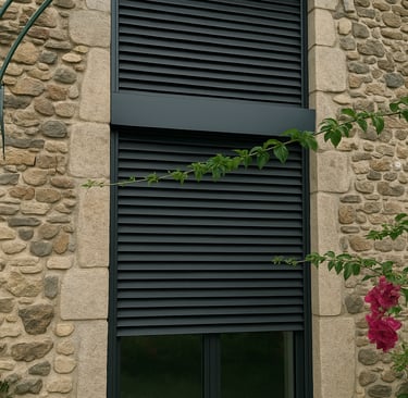 brise soleil oientable gris fermés sur une grande fenêtre d'une maison en pierre traditionnelle