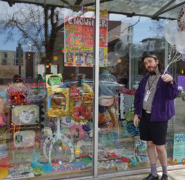 Magpie staff member holding balloons and standing in front of a storefront window filled with art