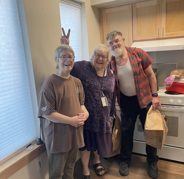 Three seniors stand together in an apartment smiling, one of them is holding up bunny ears