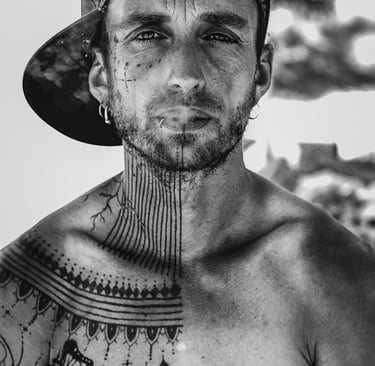 a man with tattoos on his chest and neck, a cap and smoke goes out og his mouth