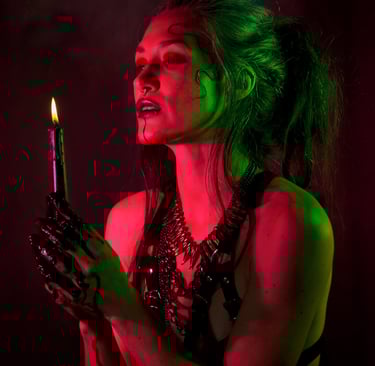 a woman wearing a harness, green and red light on her skin, holding a candle