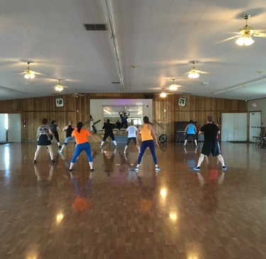 Melody teaches a Zumba class in a large dance hall.