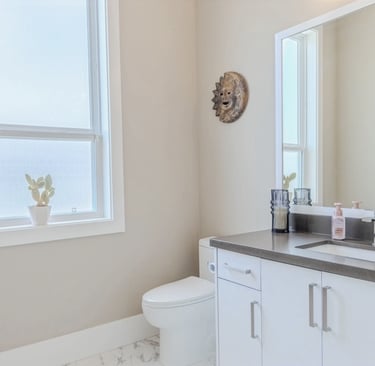 Modern bathroom interior featuring white vanity cabinets, grey countertop, and a sun-shaped wall decor.