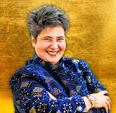 Indian woman with crossed arms smiling at camera, She is wearing a royal blue jacket with gold.